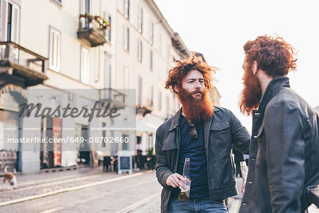 Young male hipster twins with red hair and beards talking on city street