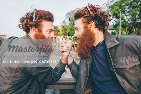 Young male hipster twins with red hair and beards arm wrestling on bridge