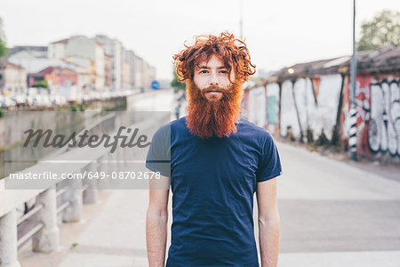Close up portrait of young male hipster with red hair and beard standing on bridge