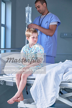 Male nurse adjusting boy patients intravenous drip in hospital children's ward