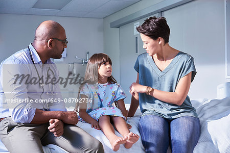 Male doctor explaining to girl patient and her mother in hospital children's ward