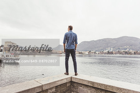 Rear view of young man standing on harbour wall looking out, Lake Como, Italy