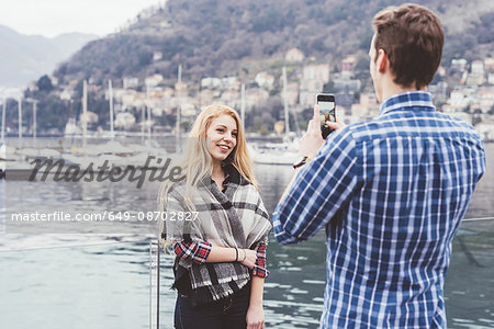 Young man on waterfront photographing girlfriend,  Lake Como, Italy
