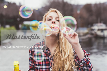 Portrait of young woman on waterfront blowing bubbles,  Lake Como, Italy