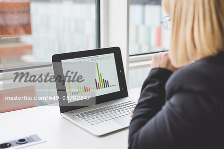 Over shoulder view of businesswoman looking at bar graph on office  laptop