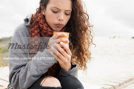 Young woman blowing into cup of coffee on cold day