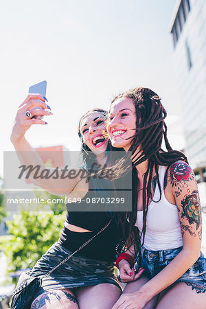 Two young women on wall taking smartphone selfie in urban housing estate