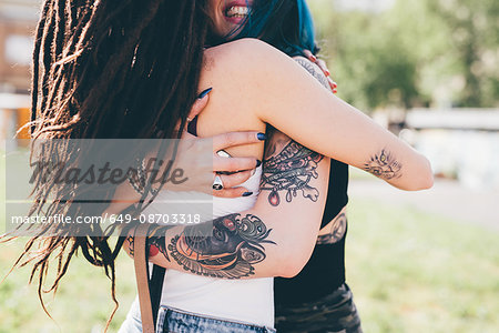 Tattooed young women hugging in urban park