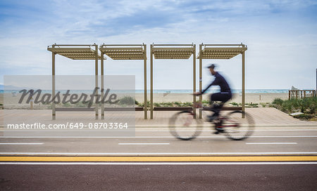 Blurred motion of cyclist cycling along coastal road, Cagliari, Italy