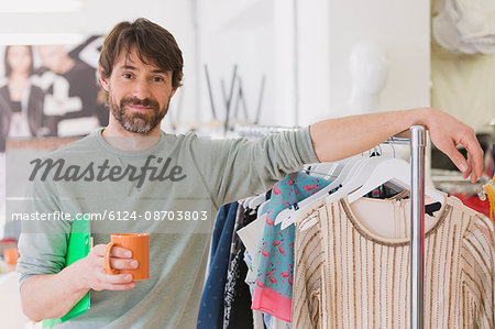 Portrait confident male fashion buyer drinking coffee leaning on rack