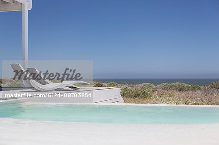 Swimming pool and modern lounge chairs overlooking ocean view under sunny blue sky