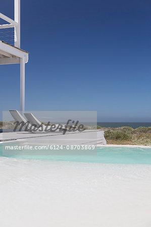 Modern lounge chairs at poolside with ocean view under sunny blue sky