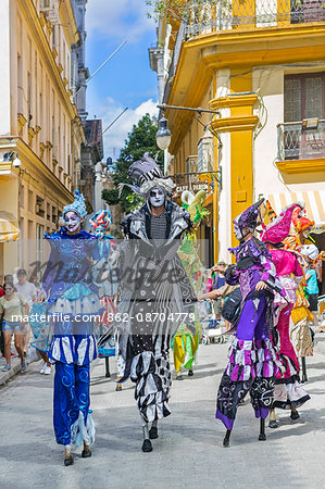 Cuba, Havana, Habana Vieja.  Colourful stilt walkers march down a street in Habana Vieja.