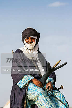 Niger, Agadez, Dabous. A Tuareg man sits on his camel using a traditional three-pronged camel saddle.