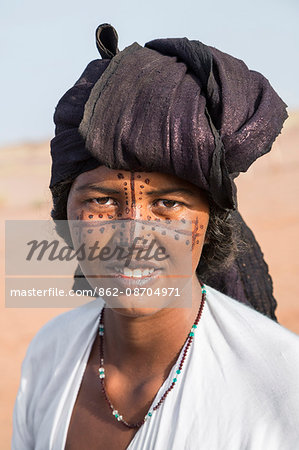 Niger, Agadez, Dabous. A Tuareg woman with painted patterns on her face. Her head scarf is coloured with indigo-blue.