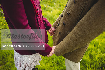 Midsection of couple holding hands while standing at park