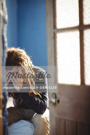 Sad hipster man sitting on bed at home