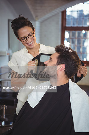 Smiling female hairdresser showing man his haircut in mirror at salon