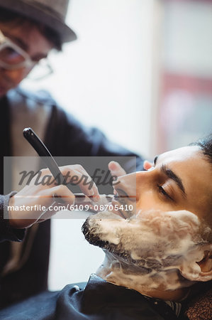 Man getting his beard shaved with razor in barber shop