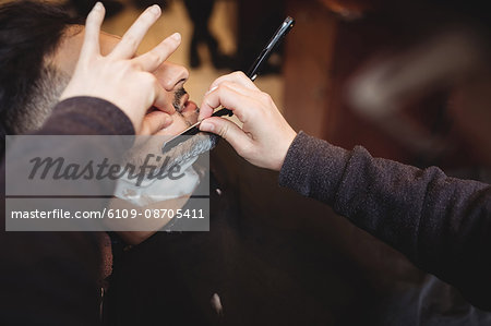 Man getting his beard shaved with razor in barber shop