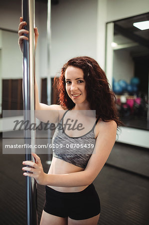 Portrait of pole dancer holding pole in fitness studio