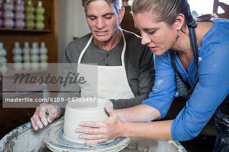 Male potter assisting female potter in pottery workshop