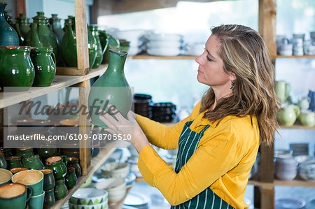Female potter placing pot on shelf in pottery workshop