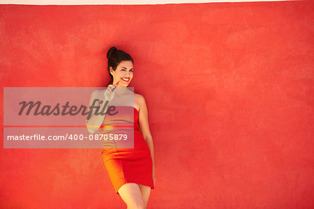 Young hispanic people smoking e-cig, pretty sensual latina woman with electronic cigarette, happy sexy girl smiling and leaning on red wall with copy space. Portrait looking at camera