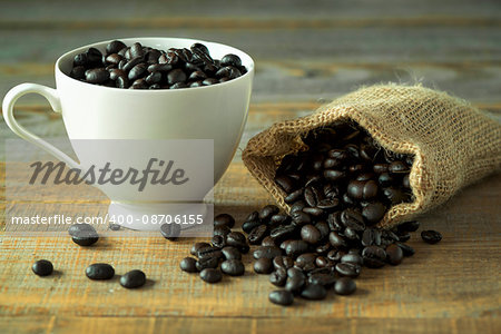 Cup and bag full of coffee beans on wooden table