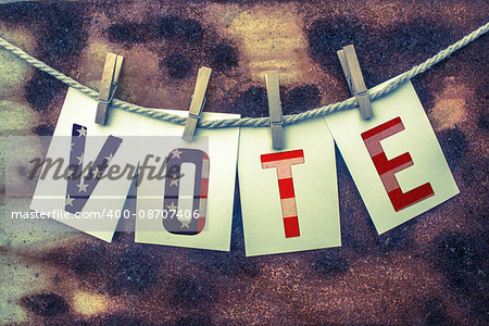 The word VOTE stamped on card stock hanging from old twine and clothes pins over a rusty vintage background.