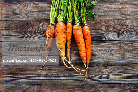 Raw carrot with green leaves on wooden background