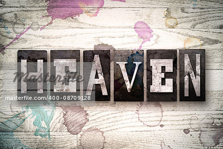The word "HEAVEN" written in vintage, dirty metal letterpress type on a whitewashed wooden background with ink and paint stains.