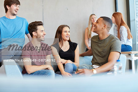 Group of young male and female students sitting on study space sofa chatting at higher education college