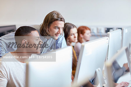 Male lecturer showing student using computer in higher education college computer room