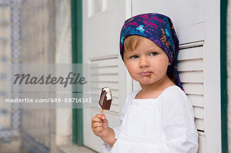 Portrait of female toddler leaning against shutters eating ice lolly, Beja, Portugal