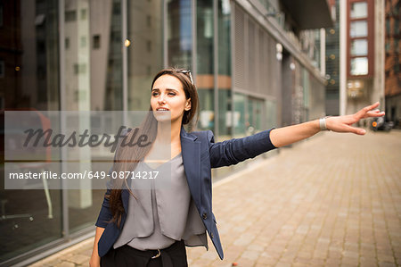 Young businesswoman hailing a cab outside office, London, UK