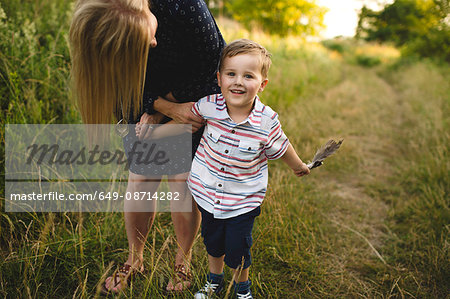 Mother bending down to son with handful of feathers in meadow