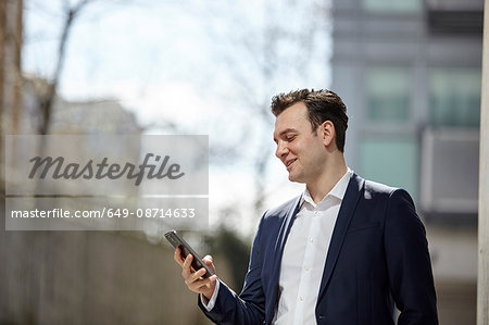 Businessman reading smartphone texts outside office, London, UK