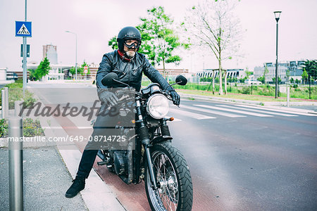 Mature male motorcyclist sitting on motorcycle on road