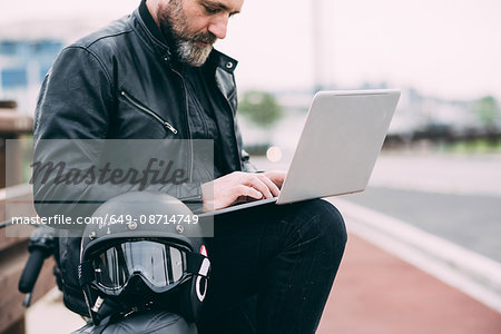 Mature male motorcyclist on roadside using laptop
