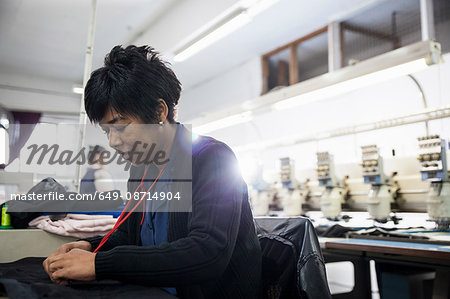 Female factory worker removing stitches from black cloth from speed stitching programmed embroidery machine in clothing factory