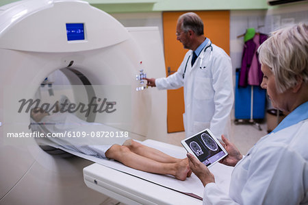 Doctor looking at brain mri scan on digital tablet and patient entering mri scan machine at hospital