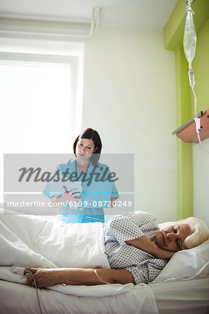Senior patient sleeping on a bed while nurse checking report in hospital