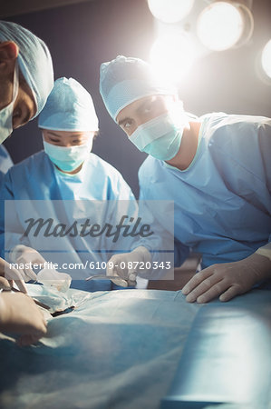 Surgeon looking at camera while colleagues performing operation in operation room