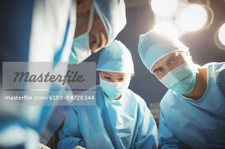 Surgeon looking at camera while colleagues performing operation in operation room