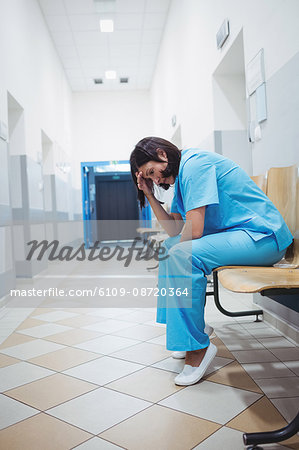 Sad nurse sitting on the chair in hospital corridor