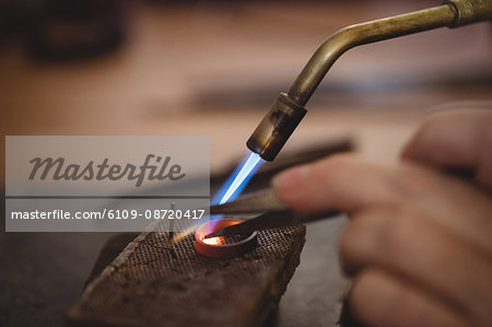 Goldsmith crafting ring by burner in workshop