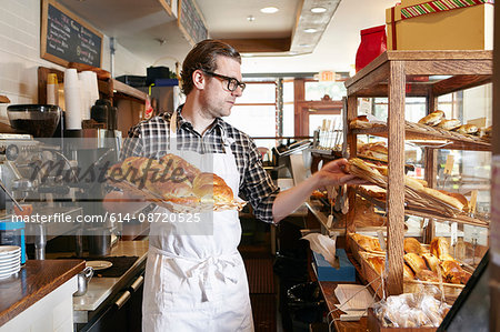 Male worker in bakery, putting fresh pastries into display cabinet