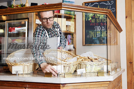 Male worker in bakery, adjusting price ticket in cabinet