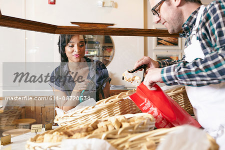 Customer in bakery pointing to baked goods, worker placing goods in bag